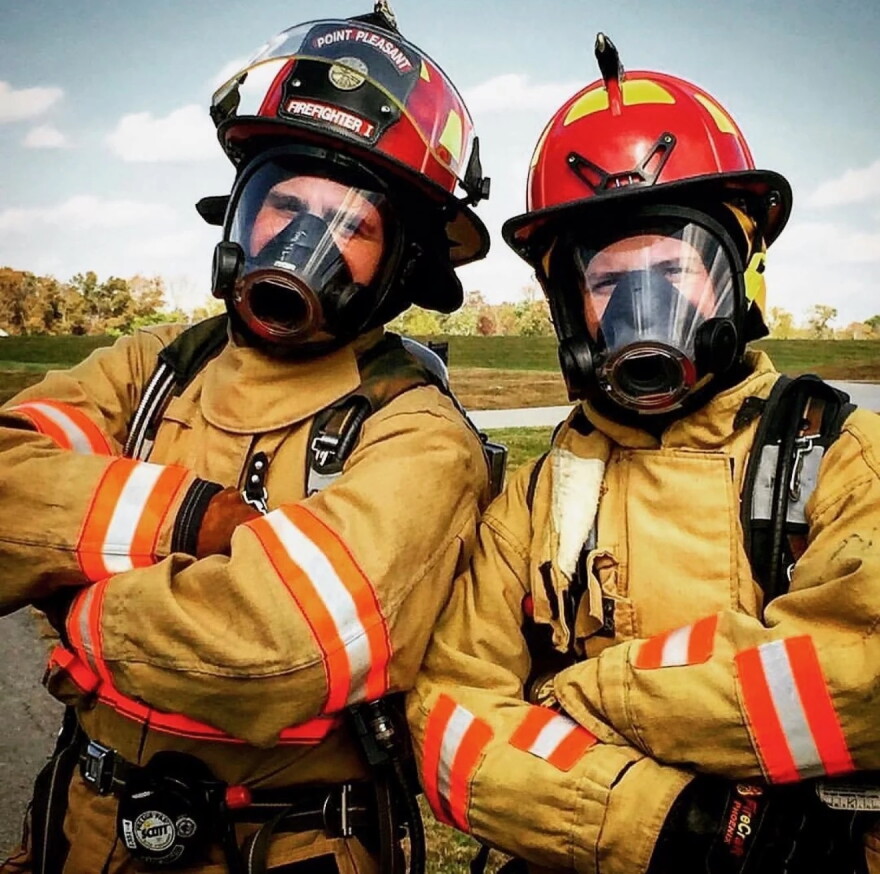 two people in full firefighter uniforms stand side by side with their arms crossed across their chests