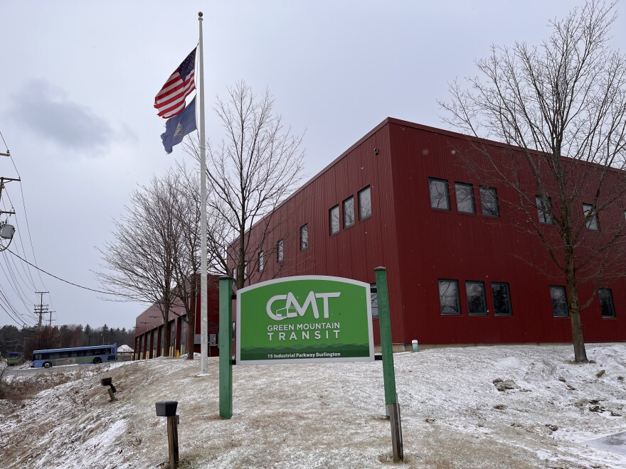 A green and white sign that reads "GMT, Green Mountain Transit" stands in front of a maroon, boxy building in Burlington, Vt.