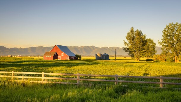 Summer sunset with a red barn and silos in rural Montana with Rocky Mountains in the background.