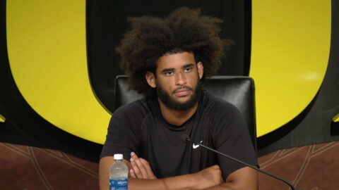 A man sits at a table in front of a microphone