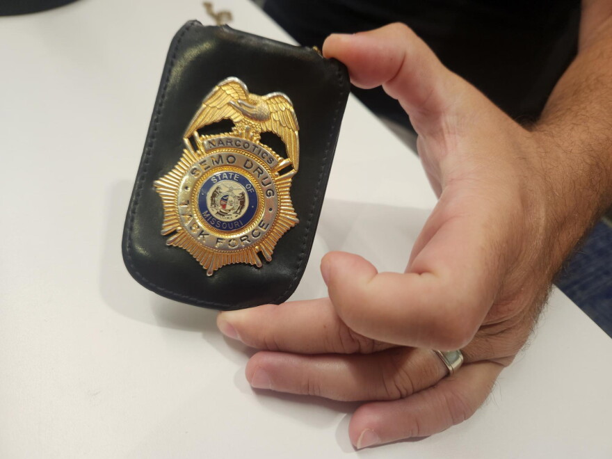 A hand holds a law enforcement badge, which reads "SEMO DRUG TASK FORCE." 