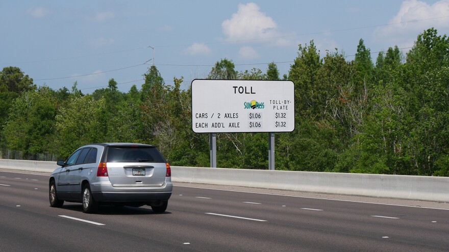 A driver in a silver vehicle on an expressway passes by a SunPass sign, on the side of the road