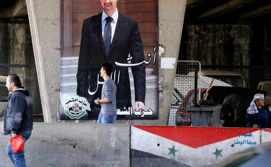 Syrian men walk past a poster bearing a portrait of President Bashar Assad in Damascus, on Feb. 27, 2016.