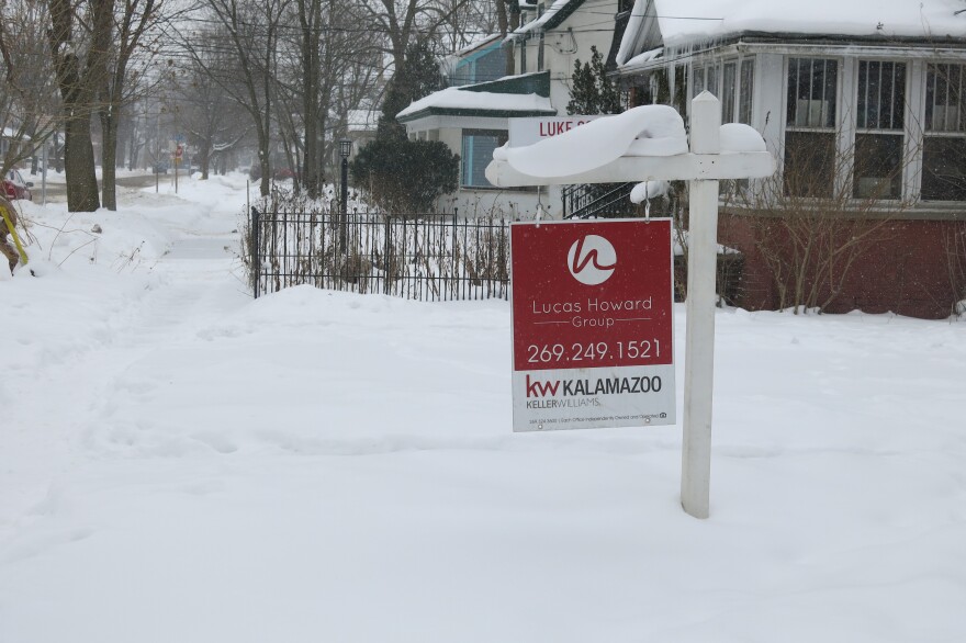 A red for sale sign in a yard a snowy neighborhood. 