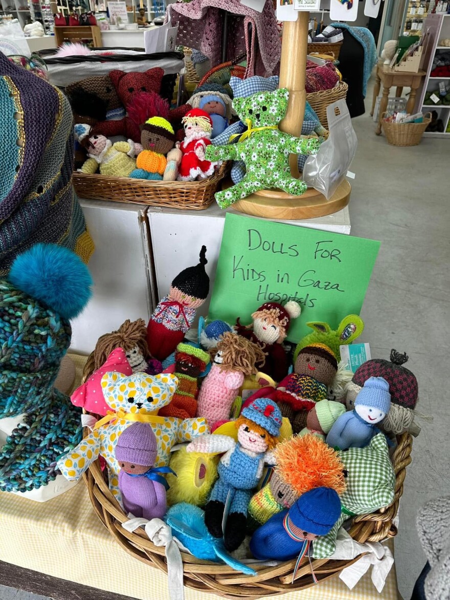Colorful toys are in a basket. A green paper says "Dolls for kids in Gaza."