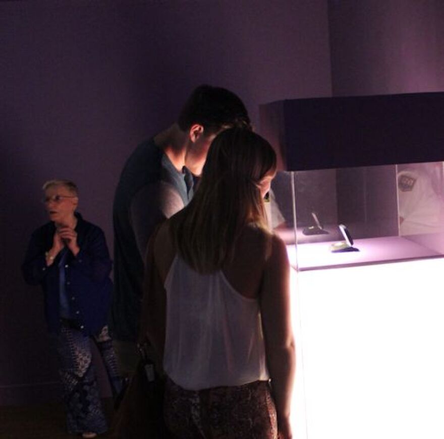 Guests view Dellinger's copy of Moon Museum chip in vitrine case during 2014 Moon Museum exhibition at Bob Rauschenberg Gallery.