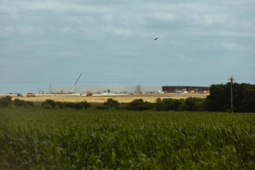 Beyond a green field covered in grass and plants is an active construction site, where OpenAI’s Stargate Milam County data center is being constructed in Burlington.