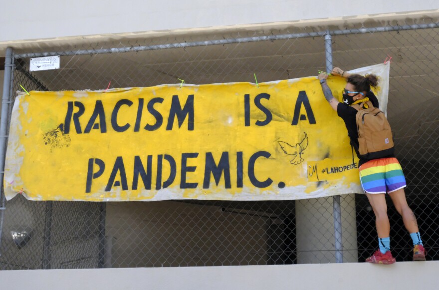 A protester hangs a sign stating "Racism is a Pandemic" at the All Black Lives Matter march , organized by black LGBTQ+ leaders, on Sunday, June 14, 2020, in Los Angeles.