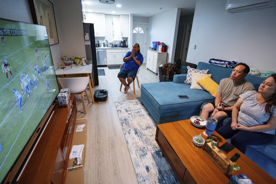 From left to right, Ron Sambrano, Tamara, and Kawehi Akiona watch football at their home, Thursday, Dec. 12, 2024, in Wailuku, Hawaiʻi. (AP Photo/Mengshin Lin)