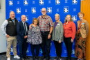 A group of adults, including Keith Cornille and Jim Davis, stand together for a photo in front of a blue backdrop. 