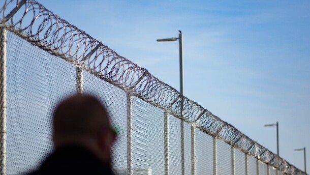 A person walks by a barbed wire fence. 