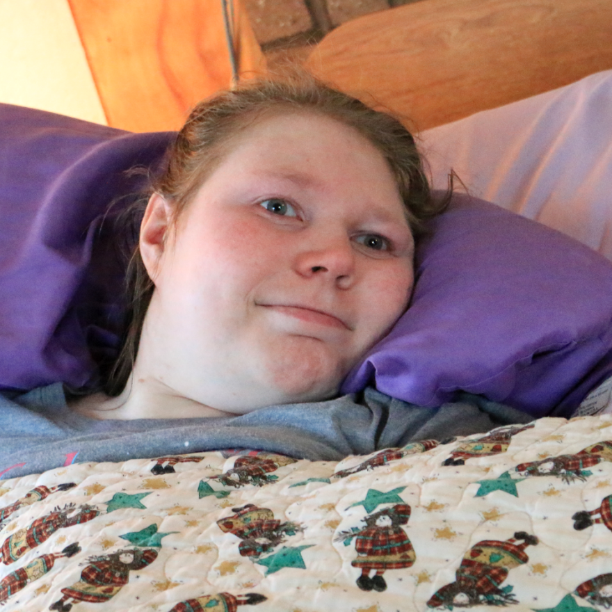 A young woman smiles from her bed.