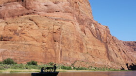 People cast fishing lines from the side of a motorboat in a shadowy river canyon.