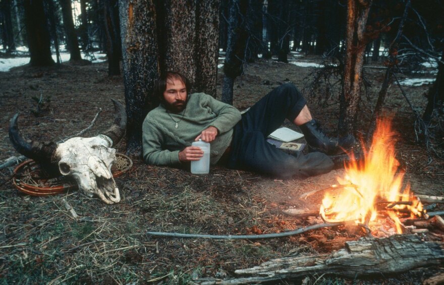 Doug Peacock sits by a fire in the Yellowstone backcountry in the late 1970s.