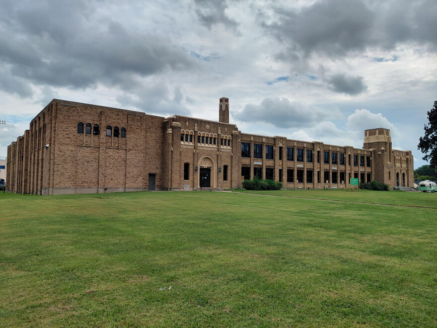 An elongated old brick school building on a slight grassy hill on an overcast day.