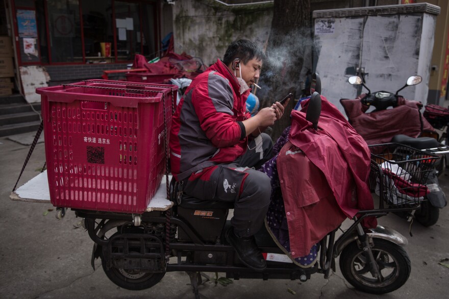 A worker with an empty cart on his scooter checks his phone.