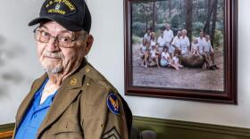 A man in a uniform stands for a portrait in front of a family photo in his home.