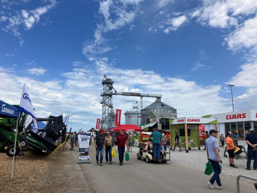 A crowd of people walk through an outdoor display of farm equipment.