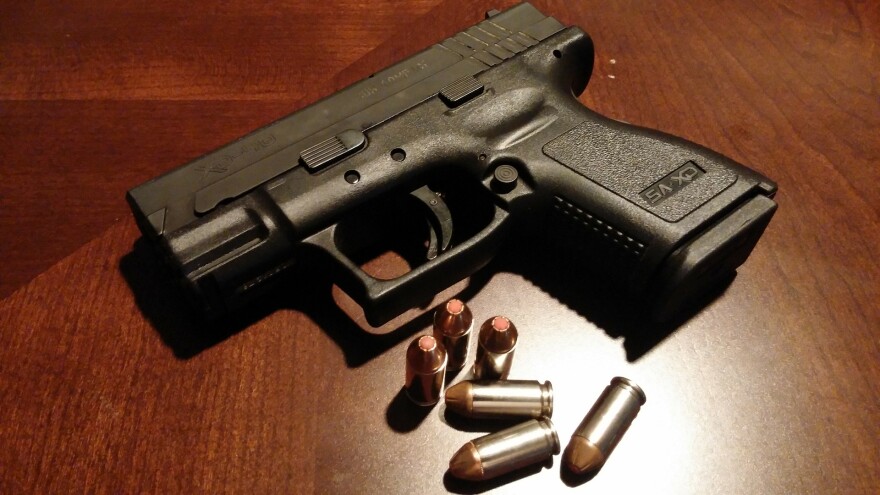 A handgun and bullets on a wooden table.