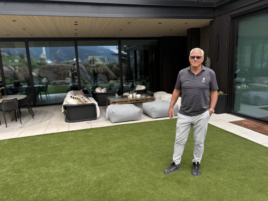 Man stands on green grass outside of a home.