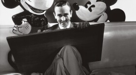 ca. October 1933, USA --- Walt Disney seated with drawing board on his lap and representations of his creations Mickey and Minnie Mouse behind. (Photo Courtesy of © Condé Nast Archive/Corbis)