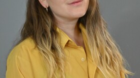 A woman wearing a yellow shirt poses on a gray background.