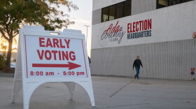A man walks in front of a beige building near a sign indicating early voting is underway.