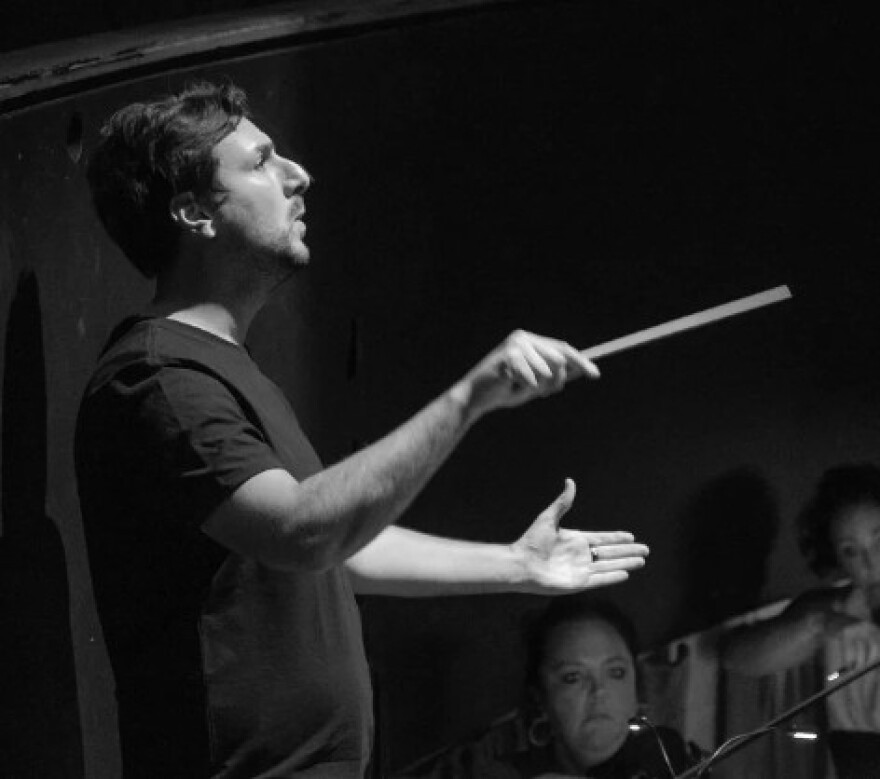 Matt Marco, Artistic Director for Buffalo Opera Unlimited, is holding a baton as he conducts an orchestra.