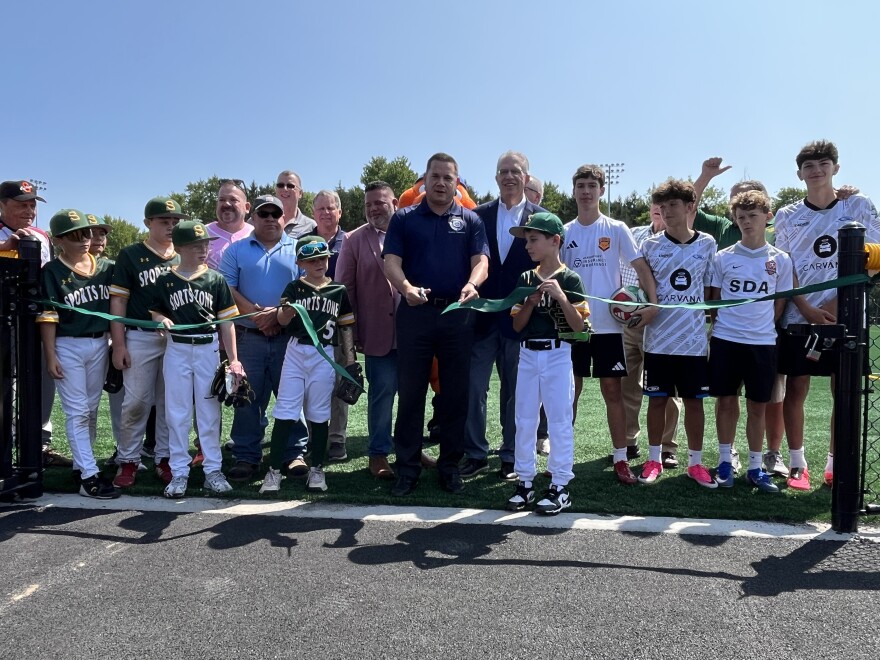 Onondaga County Executive Ryan McMahon cuts the ribbon to the field with baseball and soccer players.