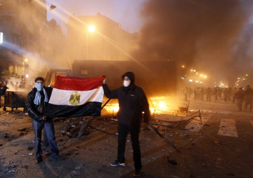 Demonstrators hold up the Egyptian flag as they stand next to a burning riot police vehicle in Cairo.