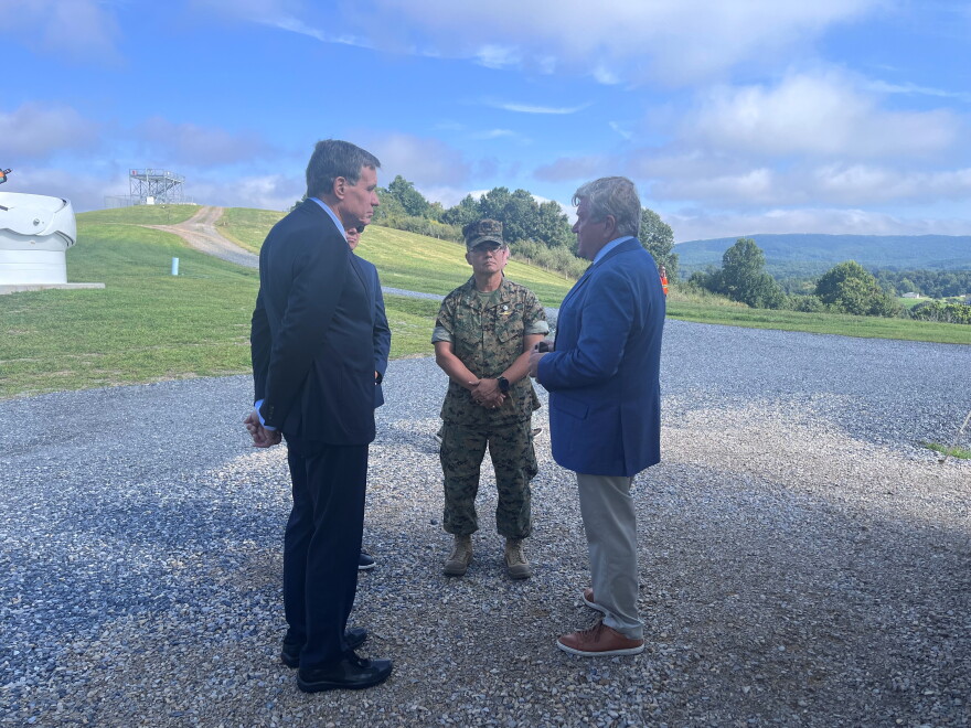 A man in a suit listens to another man wearing a blue blazer as third a man with 