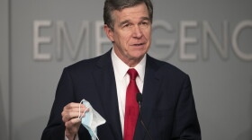 Gov. Roy Cooper holds his face mask in a press conference Monday.
