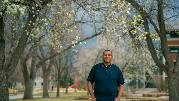 A man in a polo shirt stands between trees on a college campus