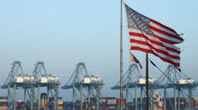 An American flag flies nearby with shipping containers stacked at the Port of Los Angeles in the background, which is the nation's busiest container port.