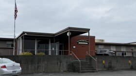 A single story building with stairs leading to the front door. It has a red brick facade and an American flag outside. 