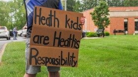 A person holds a sign that reads "Heath kids are Heath's responsibility" in front of a municipal building. 