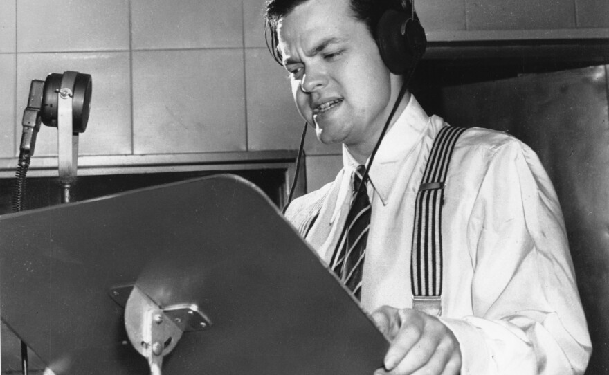 Orson Welles delivering a radio broadcast in 1938, the same year he aired his <em>War of the Worlds</em> fake news program.