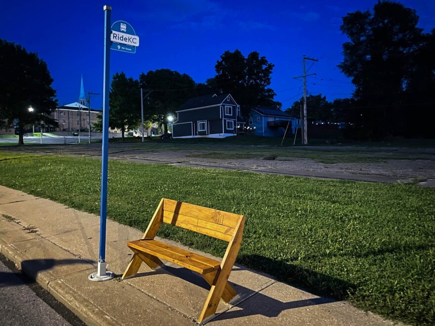 A wooden bench sits on a sidewalk next to a bus stop pole