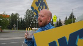 Gubernatorial candidate Jonathan Kreiss-Tomkins hoists a campaign sign on the morning of Aug. 18, 2026, Alaska’s primary election day.