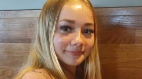 Closeup of teenage girl with straight blond hair and smiling while seated in front of a wood backdrop 