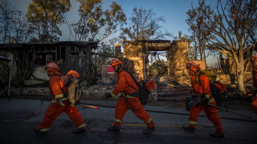 Inmate firefighters walk past a burnt building Monday in Brentwood, Calif., where the Getty Fire destroyed several homes and forced a partial shutdown of the busiest highway in the country.