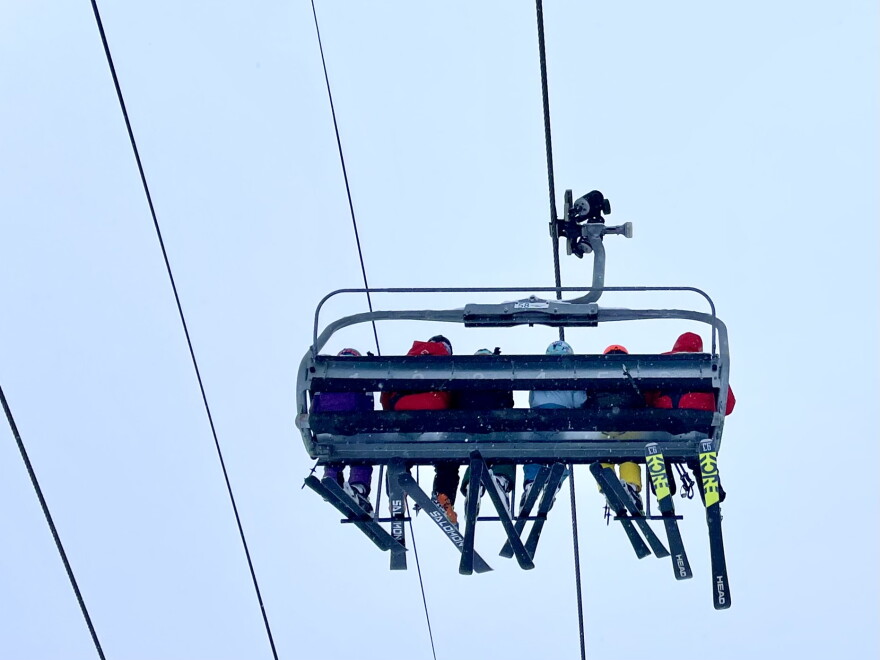 Skiers ride a chairlift on a cloudy day in Snowmass Village