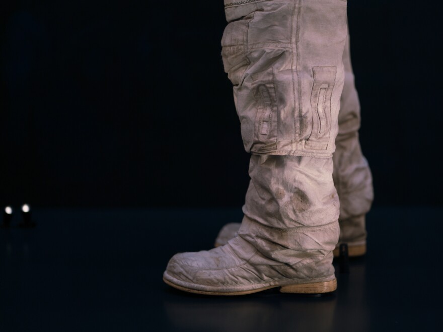 The thighs, knees and boots of the spacesuit are stained with lunar dust.