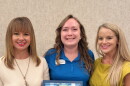 Three women in business casual attire pose with a plaque highlighting Leadership Northwest Florida Legacy for Kelsi Jackson in the middle.