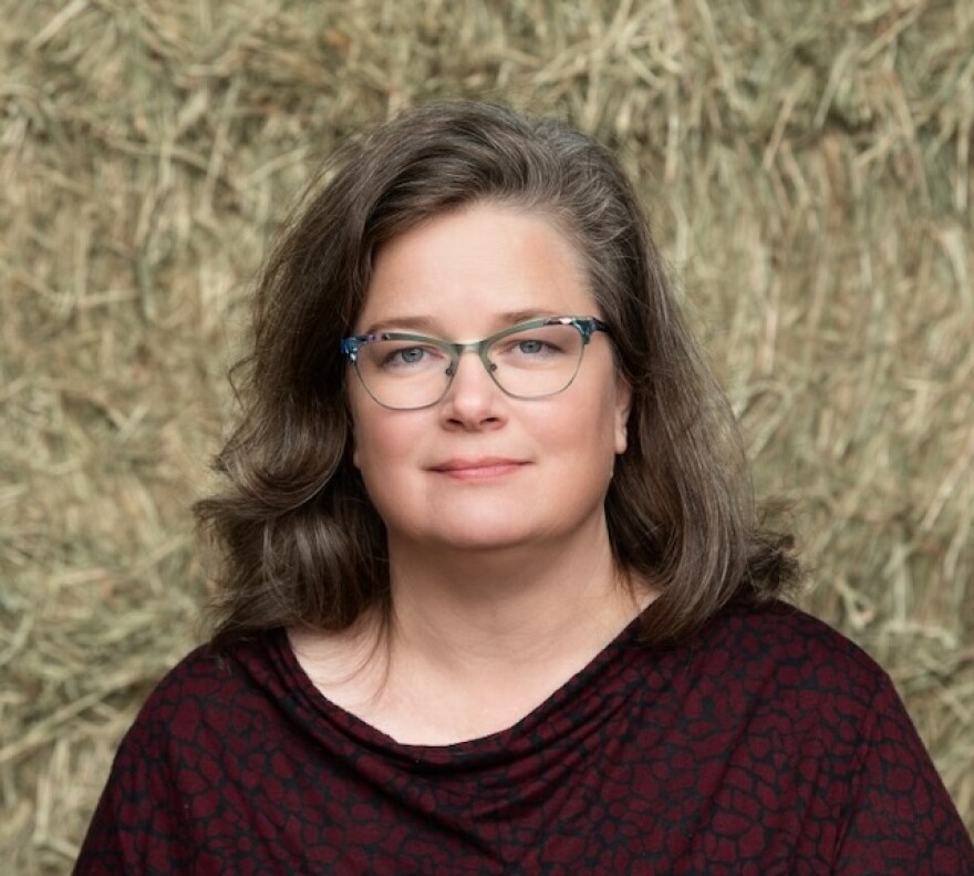 A headshot of Sarah Lloyd. She is standing in front of hay and has on glasses.