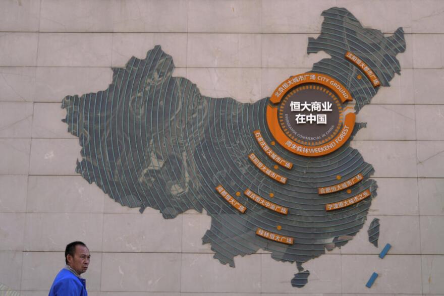 A custodian stands near a map showing Evergrande development projects in China on a wall in an Evergrande city plaza in Beijing, Tuesday, Sept. 21, 2021. (Andy Wong/AP)