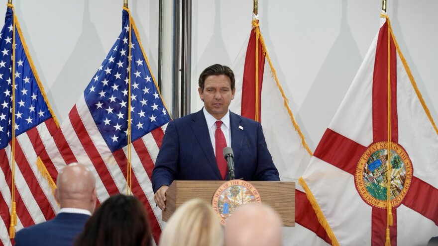 Governor Ron DeSantis speaking at a podium with flags behind him 