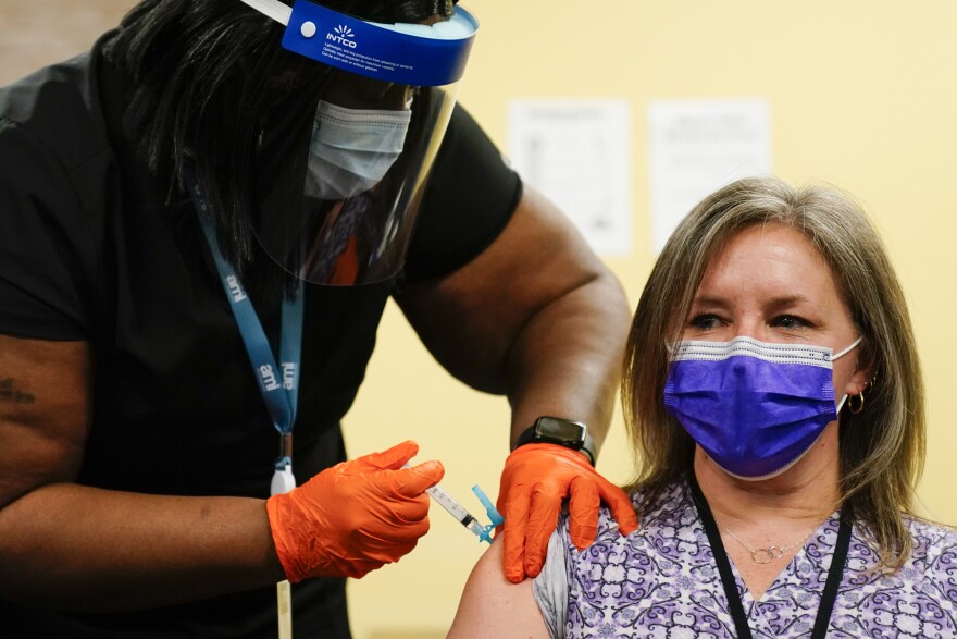 A masked woman receiving a COVID shot in the arm from a nurse