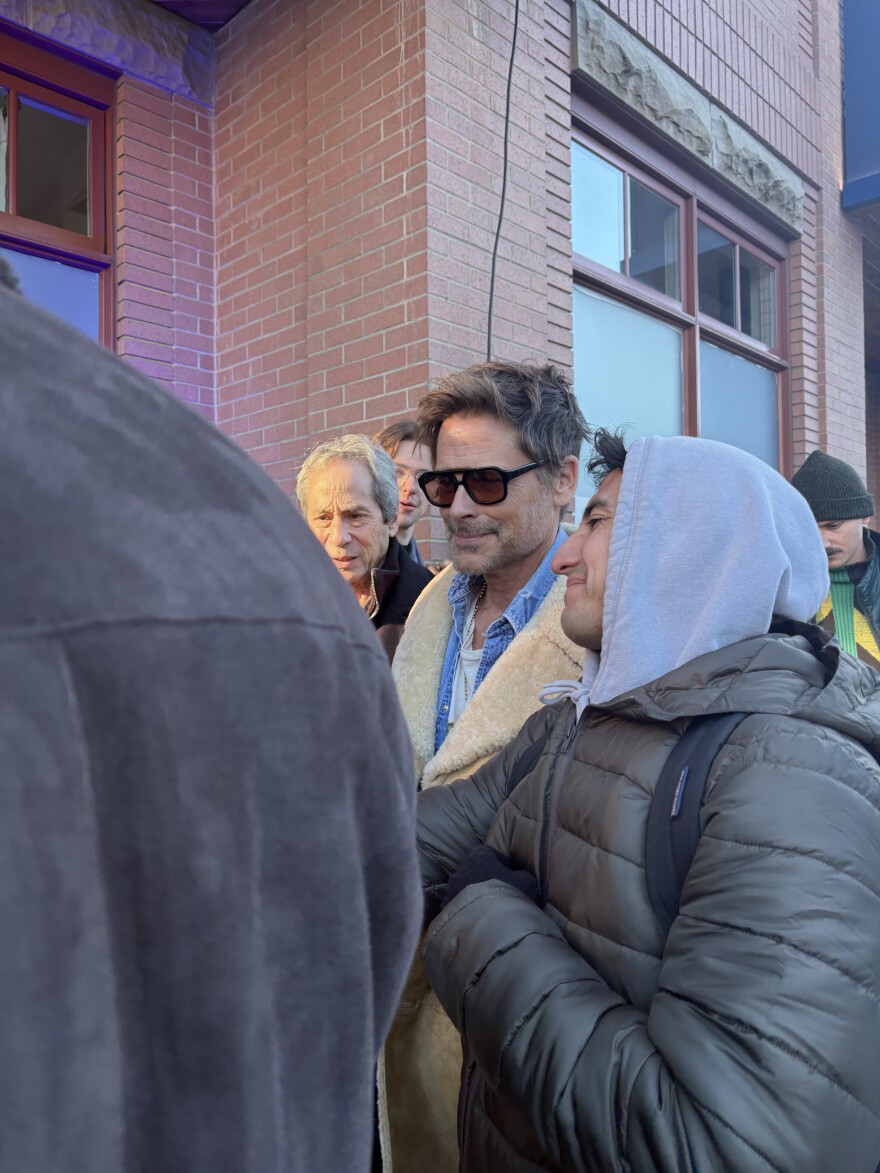 A man wearing sun glasses walks through a crowd of people. 