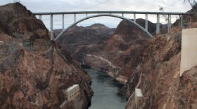 A dark, wide river flows through a steep canyon with a bridge crossing it